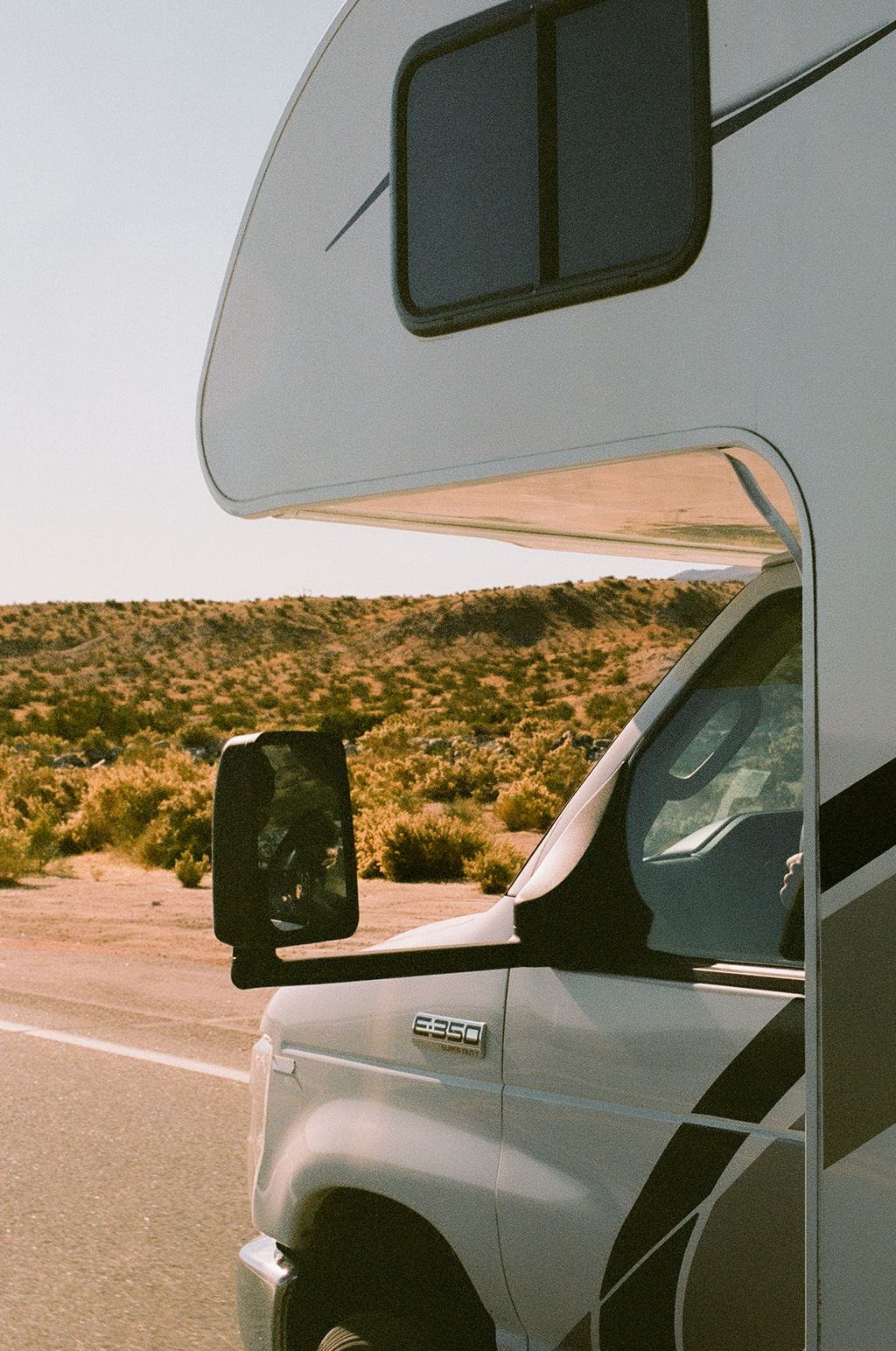 Close up image of the cab of an RV driving down a road next to a large field