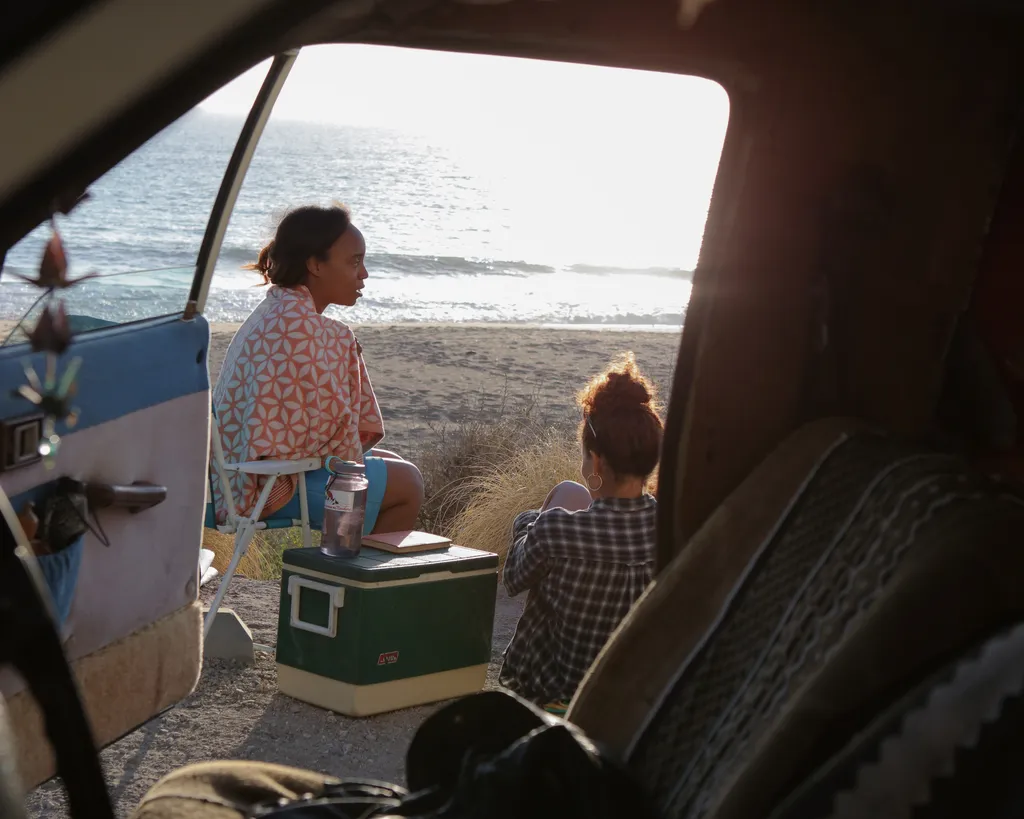 Two girls relaxing on a beach through the lens of someone sitting in an RV