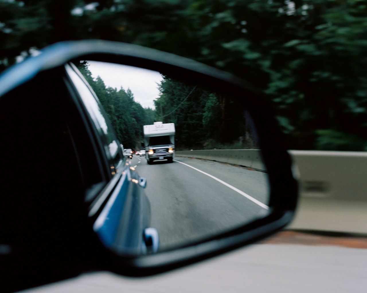 Close up of a vehicle's side mirror showing the road and mountains behind the vehicle