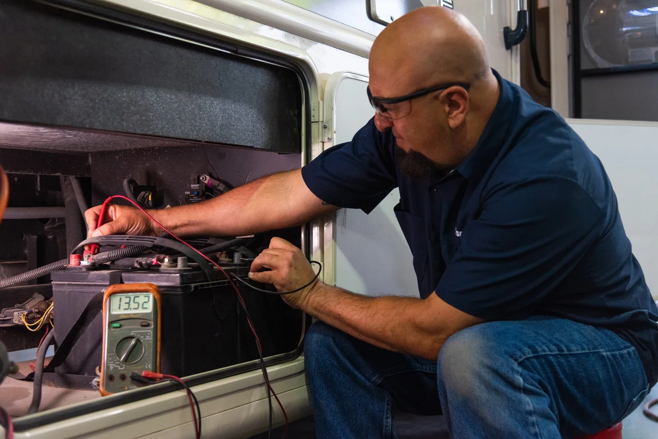 Technician testing RV battery voltage with a digital multimeter.
