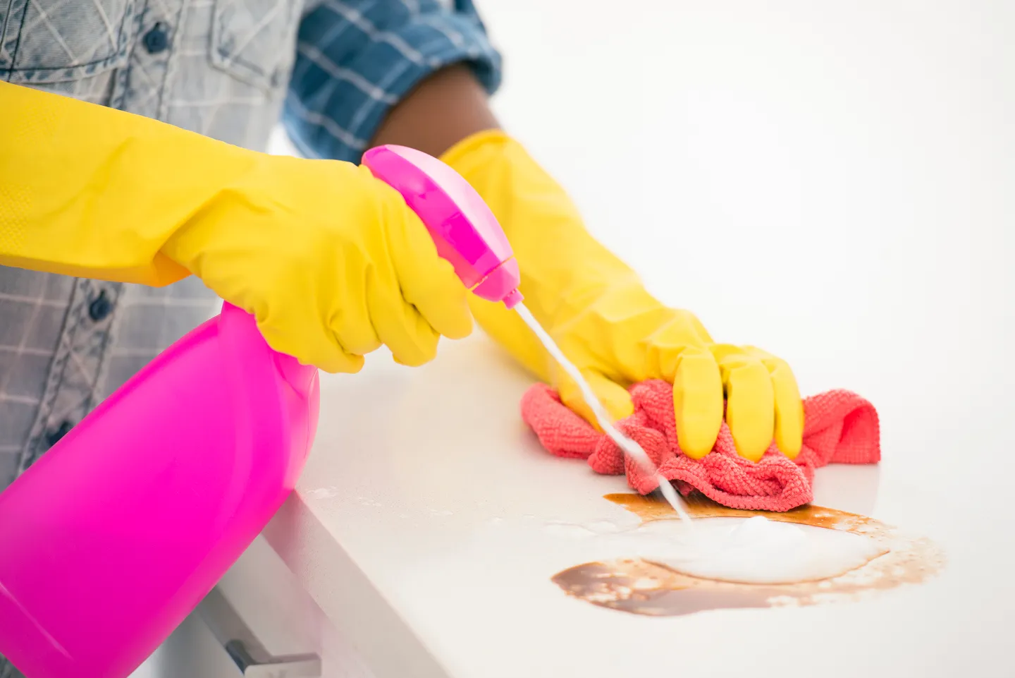 Hands in yellow gloves spraying cleaner on a surface.