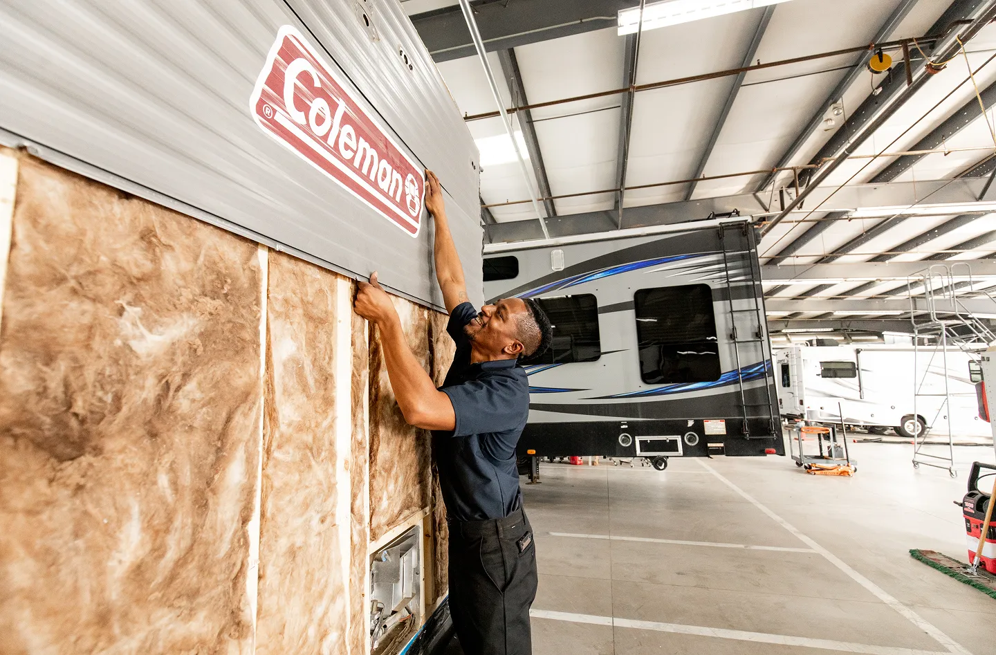 Technician repairing the exterior wall of a travel trailer inside an RV service center.