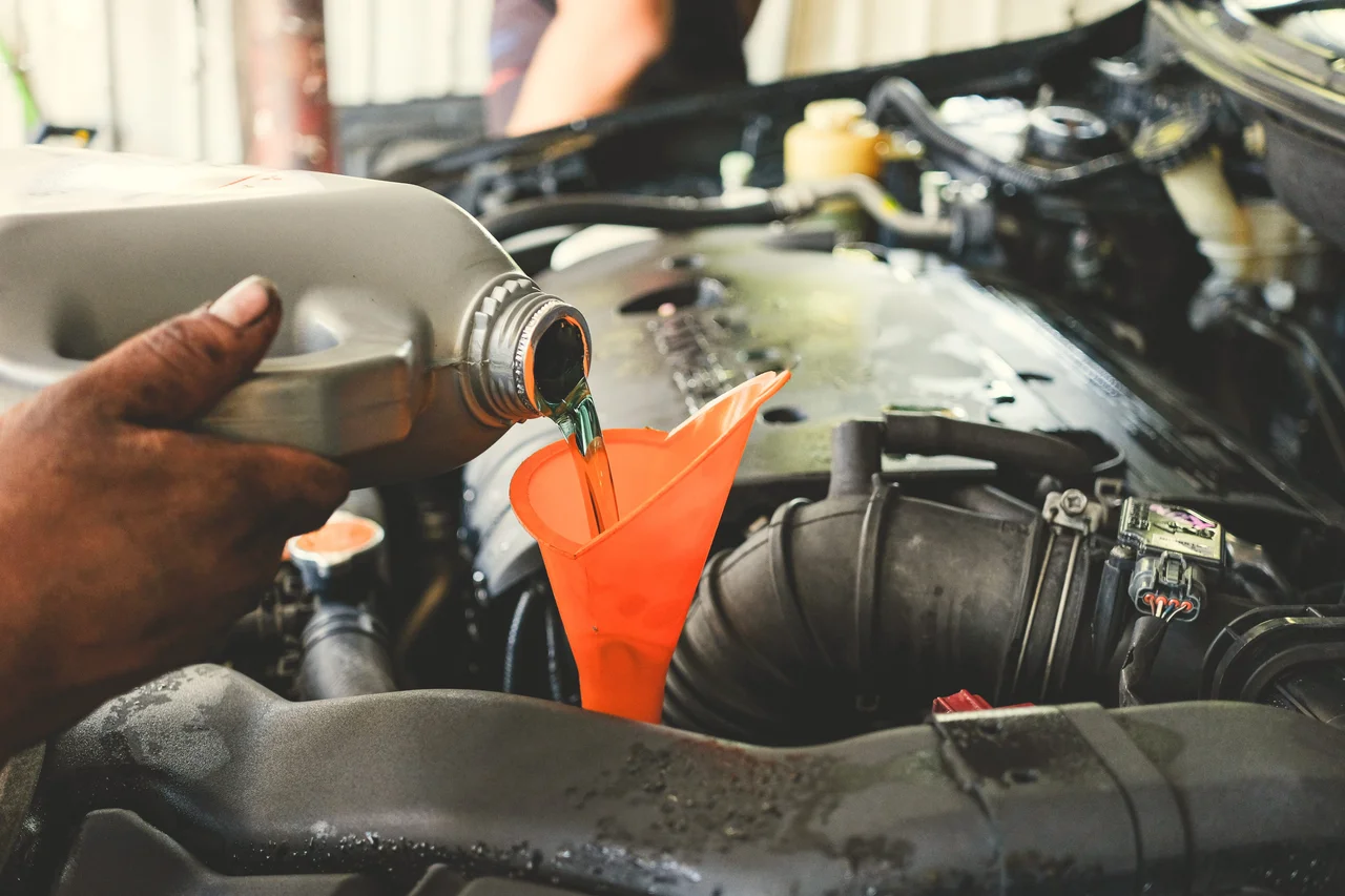 Mechanic pouring fluid into an engine compartment.