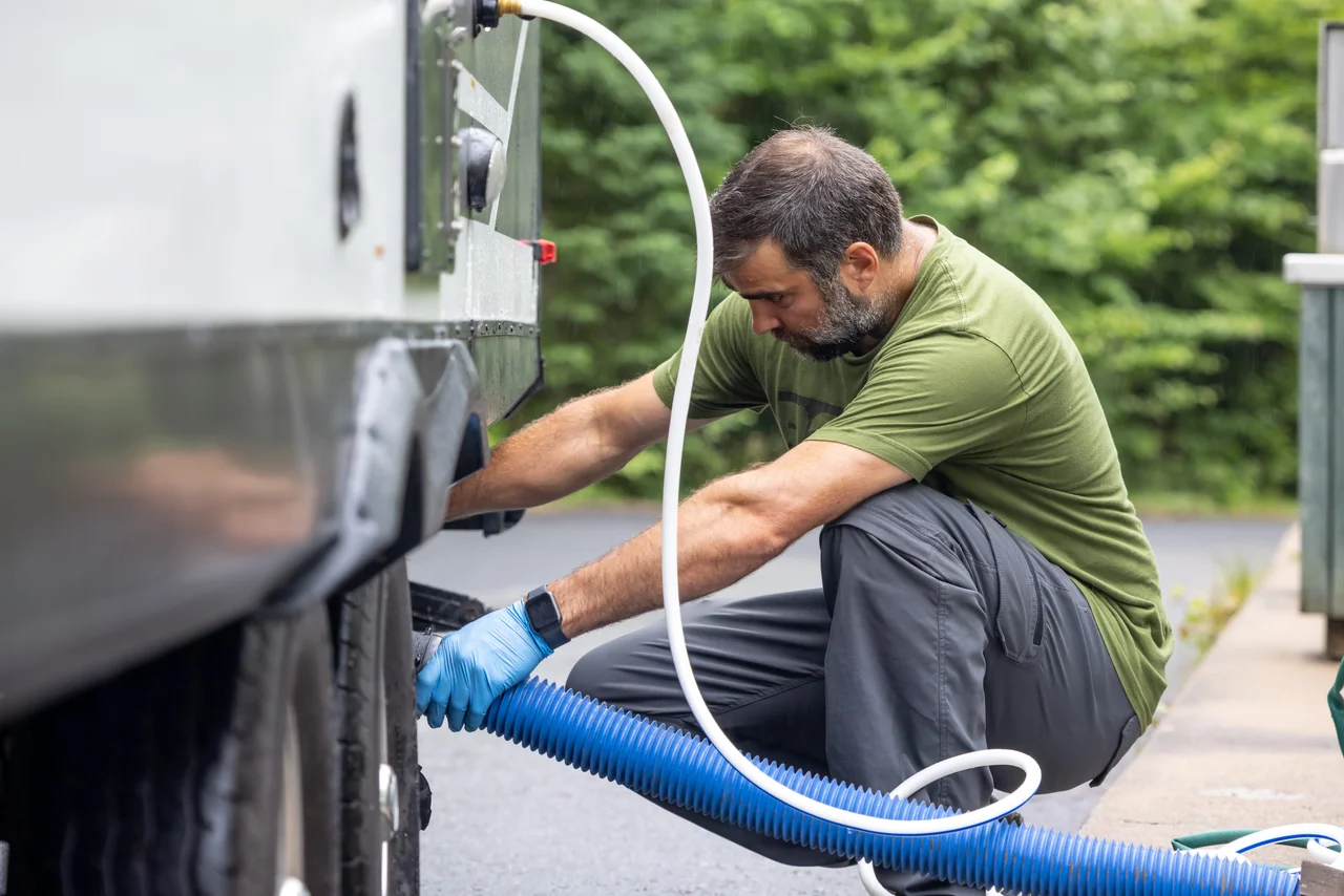 Person connecting an RV sewer hose for wastewater tank maintenance.