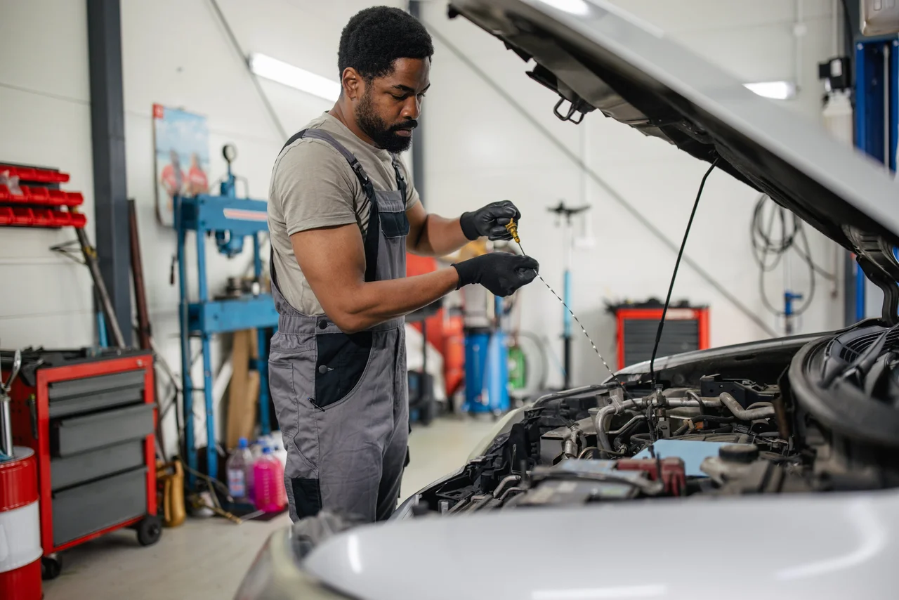 Technician checking engine oil level with a dipstick during vehicle maintenance.