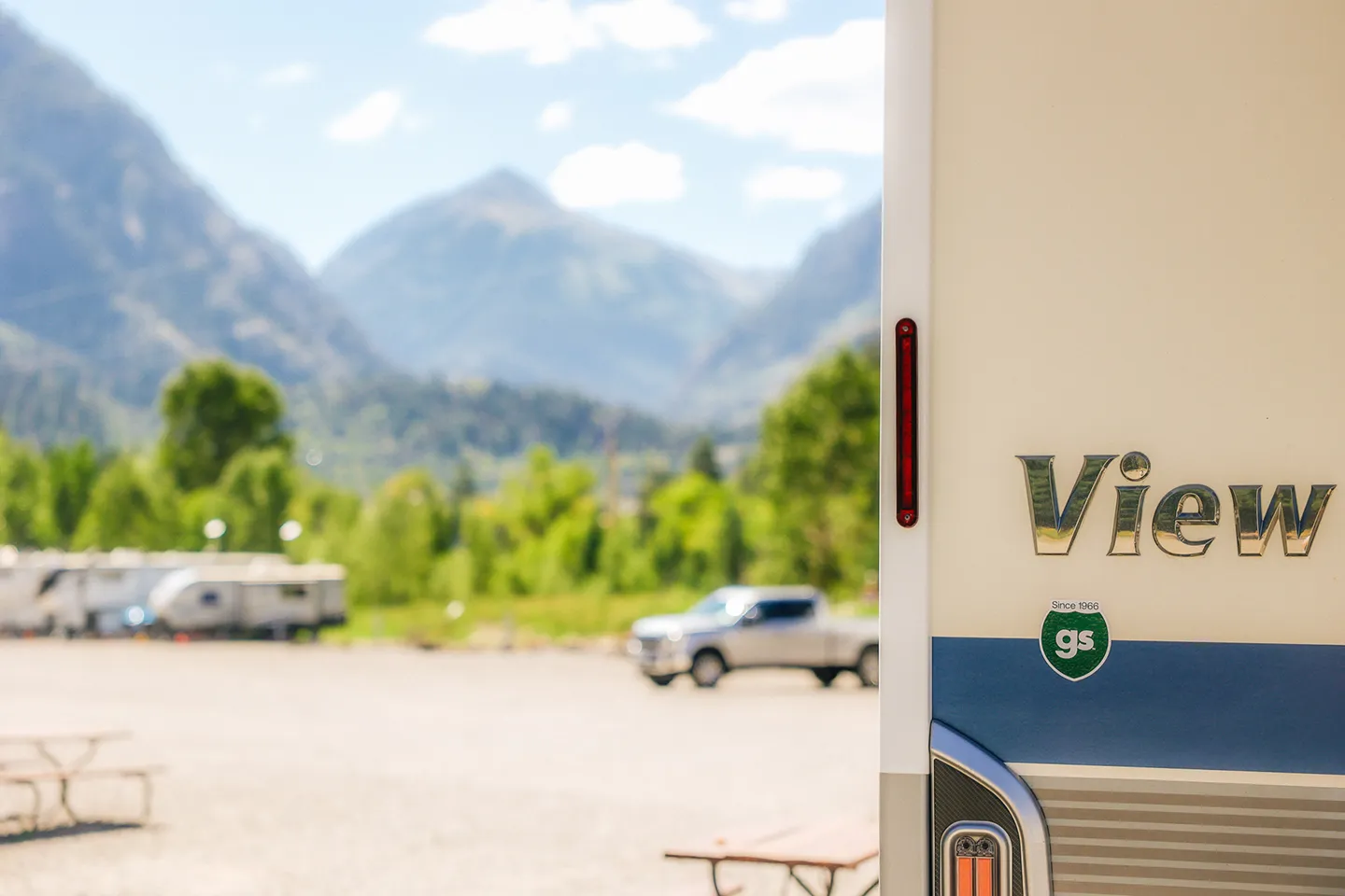 RV parked at a campground with mountains and trees in the background.