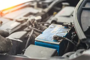 Old blue automotive battery with cable clamps attached, mounted in a dusty engine compartment