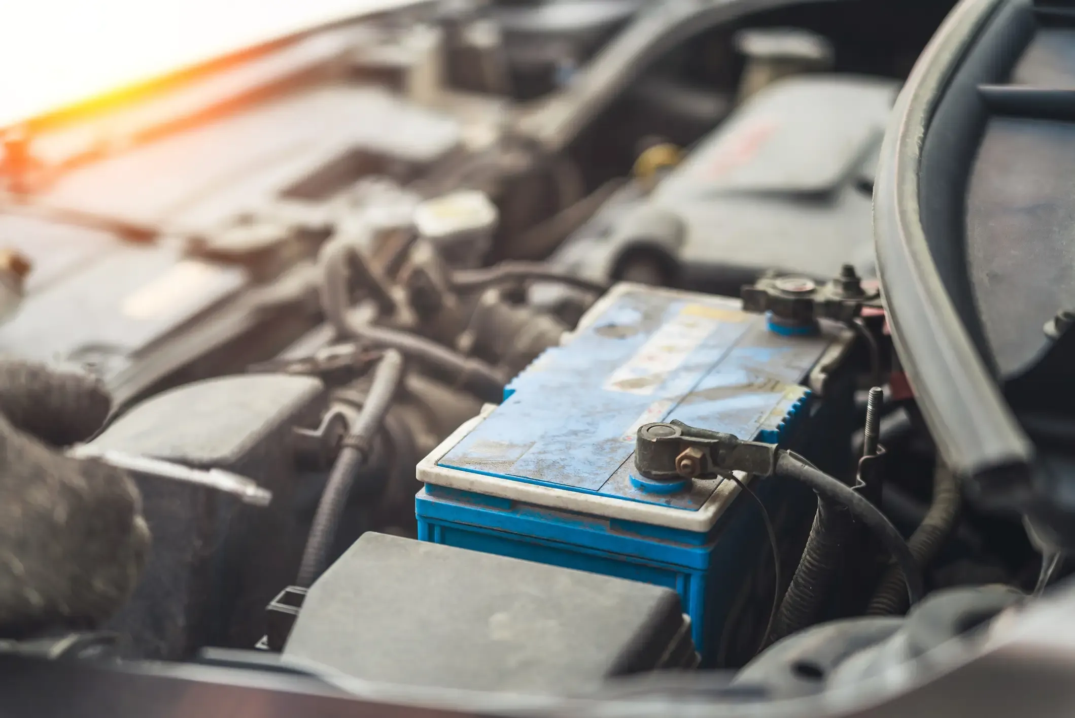 Old blue automotive battery with cable clamps attached, mounted in a dusty engine compartment