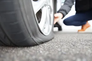 Close-up of a punctured tire on an alloy wheel with a person inspecting it on the roadside