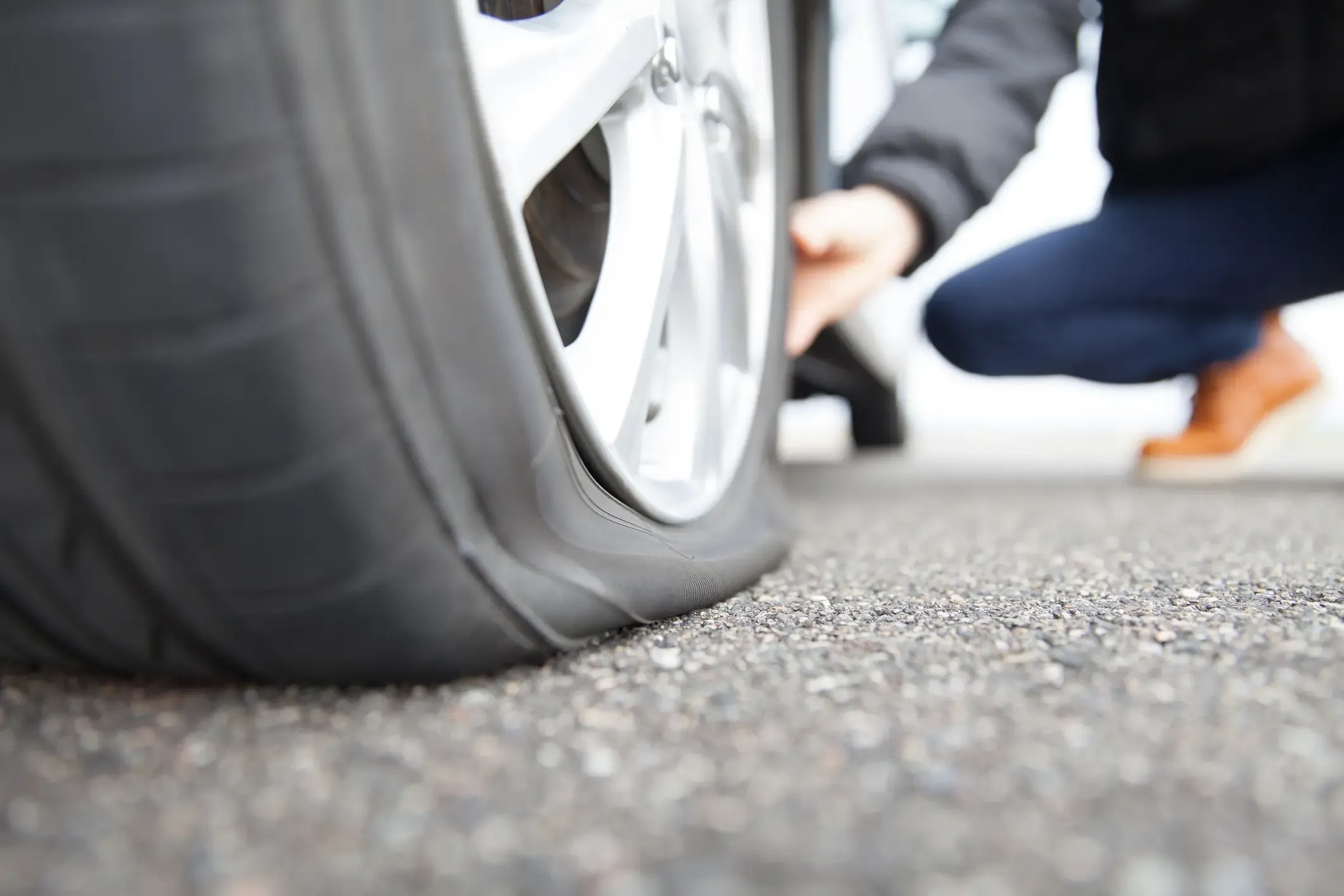 Close-up of a punctured tire on an alloy wheel with a person inspecting it on the roadside