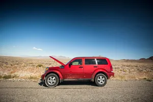 Red SUV with its hood up, broken down on a remote desert roadside with mountains in the distance
