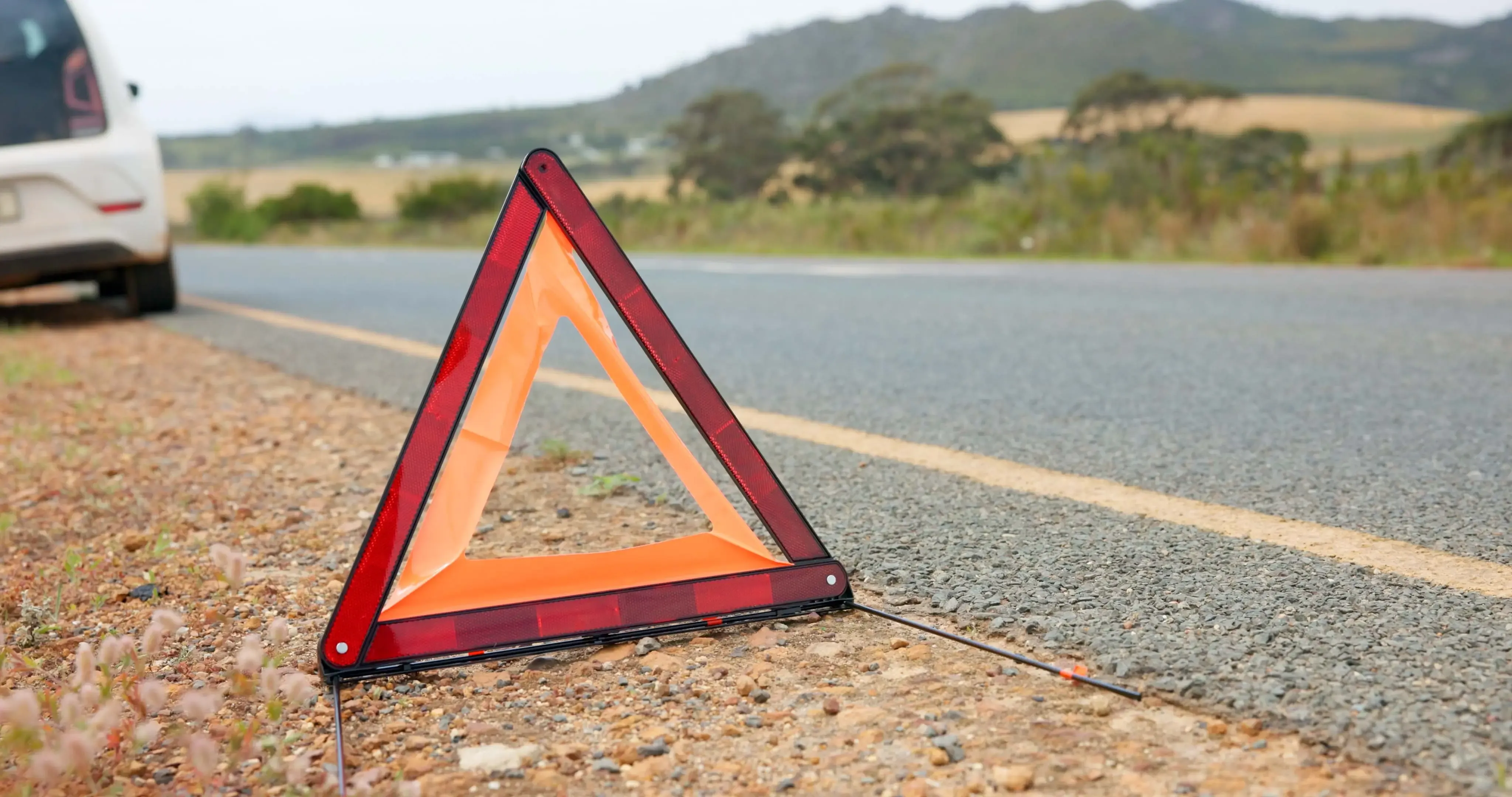Reflective warning triangle set up on the roadside behind a stopped white car on a rural road