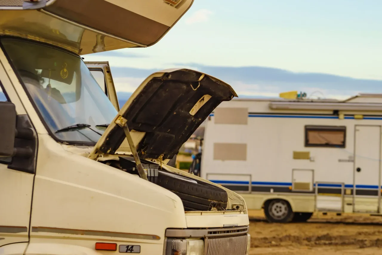 An RV's hood up with another RV in the background. 