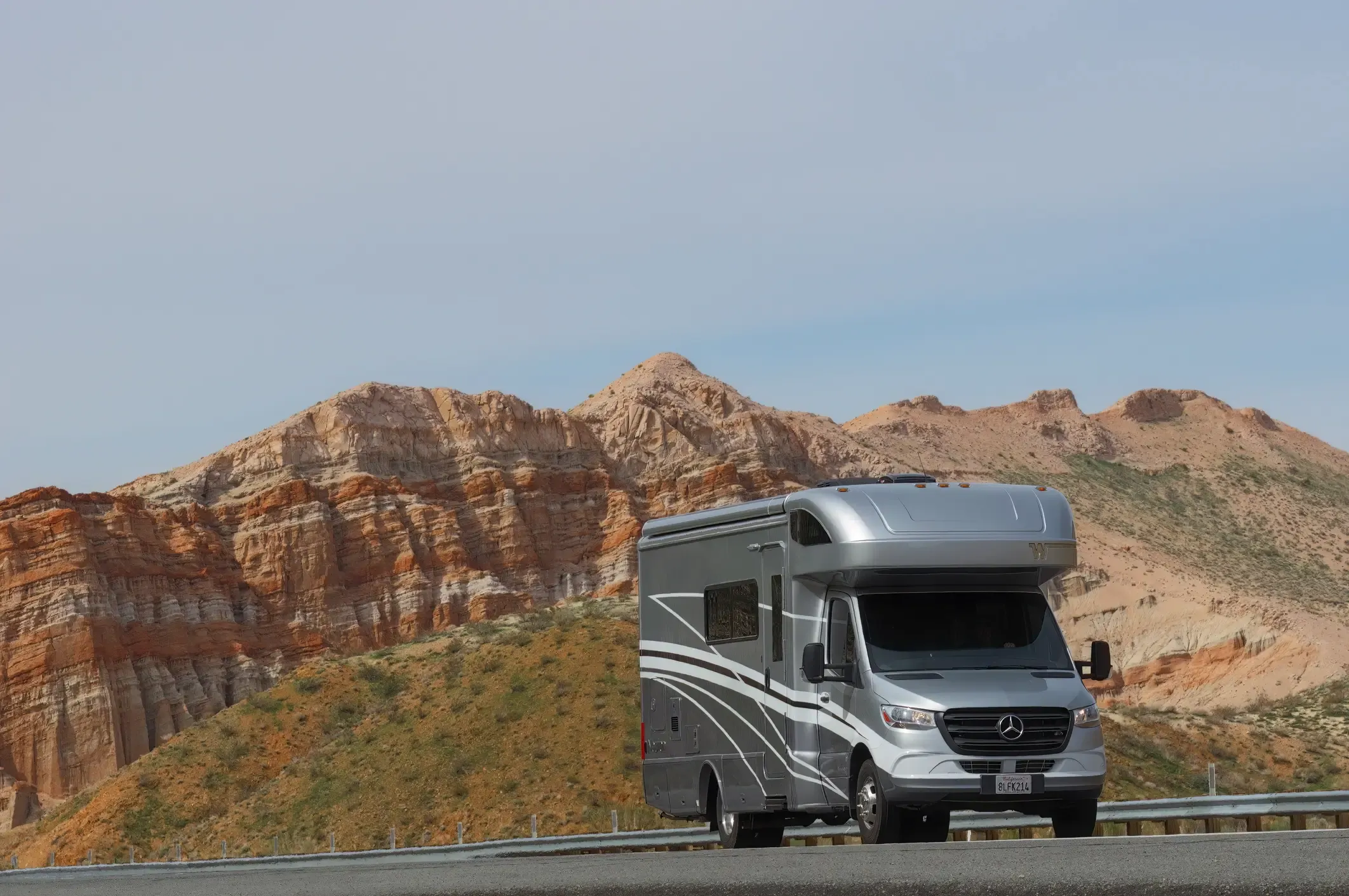 Silver Class C motorhome parked on a desert road in front of dramatic red rock cliffs