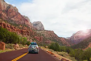 SUV loaded with bikes and camping gear driving a scenic canyon road through red rock country