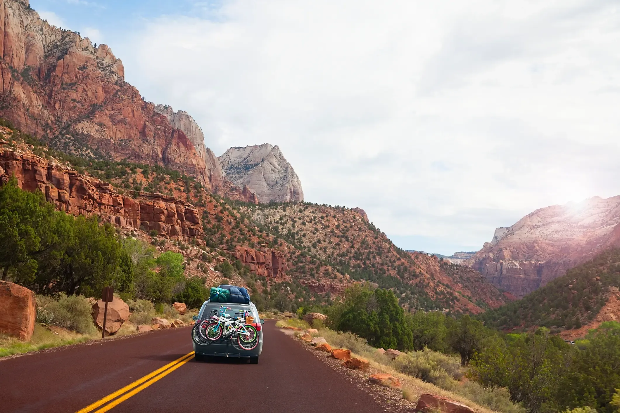 SUV loaded with bikes and camping gear driving a scenic canyon road through red rock country