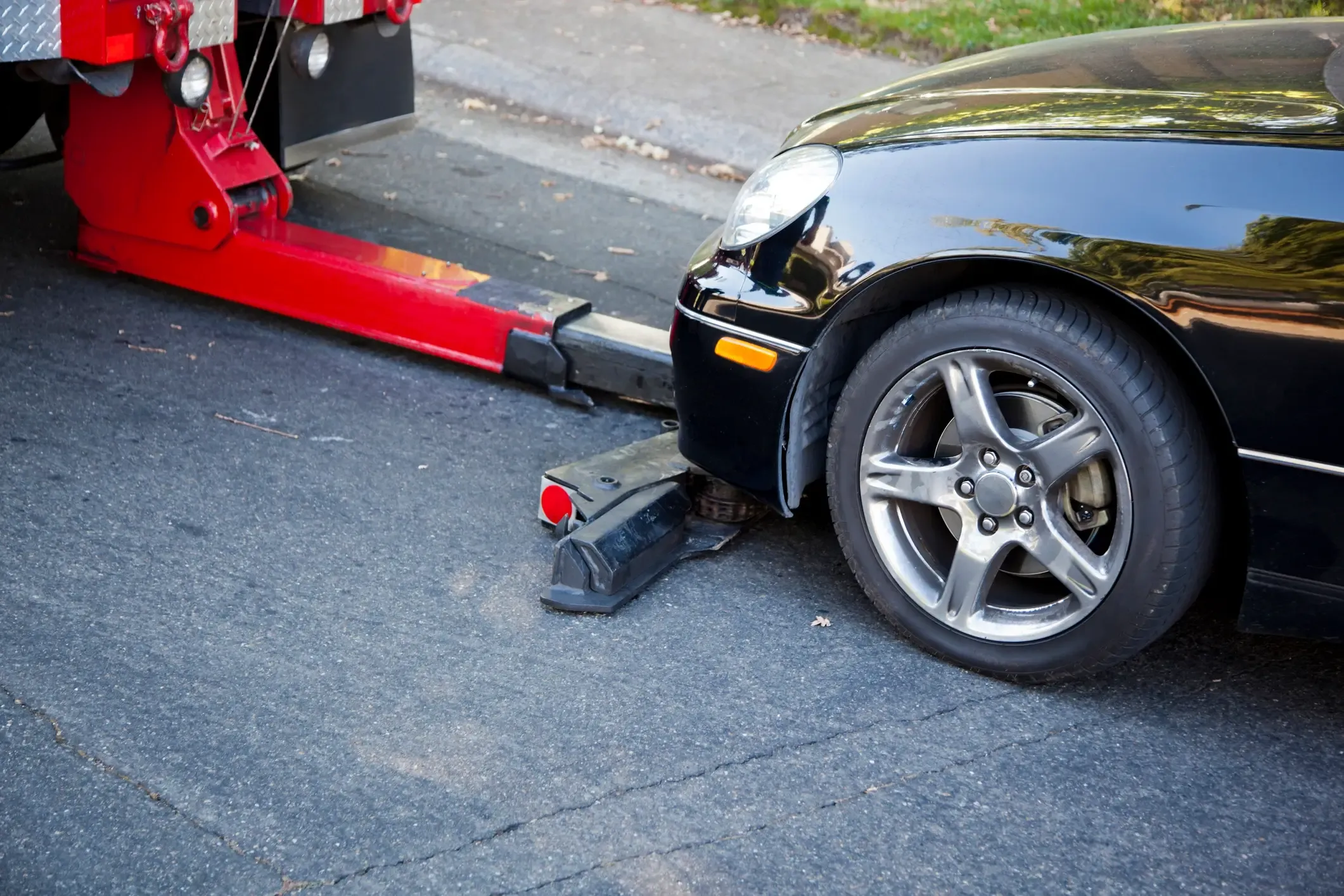 Red tow truck's wheel-lift arm hooking up the front wheel of a black car for towing