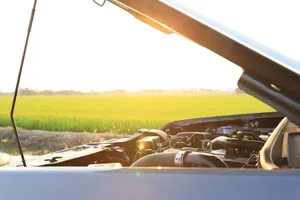 Raised hood and exposed engine of a broken-down vehicle stopped by a rural field