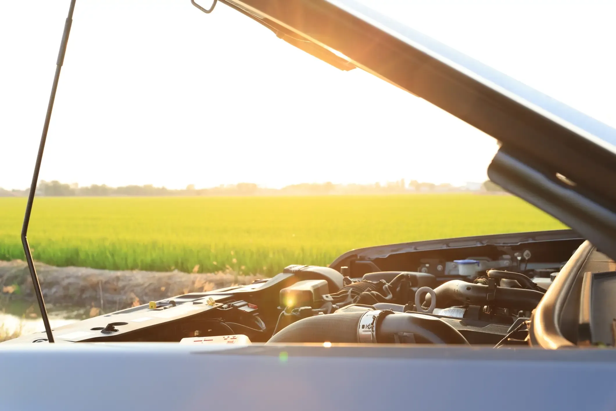 Raised hood and exposed engine of a broken-down vehicle stopped by a rural field